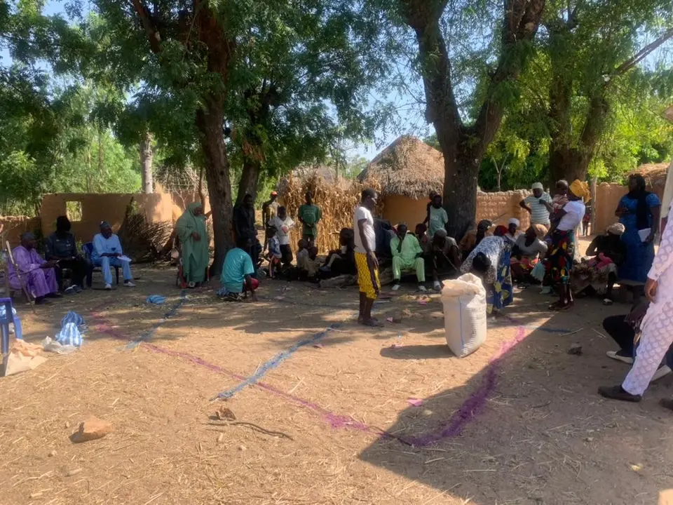 Community members gathered under trees for a community meeting